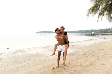 Fototapeta na wymiar Man walking on the beach piggyback riding a woman