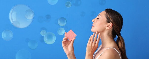 Beautiful young woman with soap bar and many bubbles on blue background