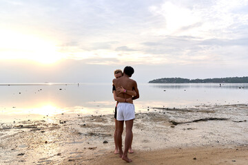 Multicultural couple embracing while standing next to the sea during sunset