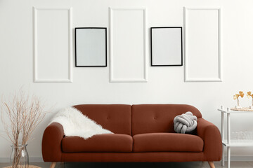 Soft sofa near light wall with blank frames