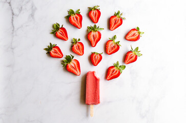 Strawberry slices arranged around a red strawberry popsicle on a white marble background