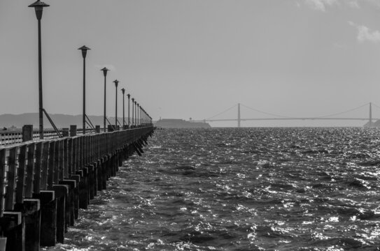 Dramatic black and white image of the Berkeley Marina, with the pier and piers lights fading into the horizon, and Golden Gate Bridge in background.