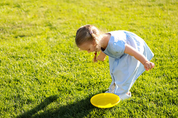 Cute little girl in dress playing frisbee in park