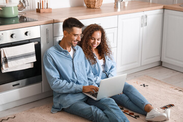 Young couple using laptop on floor in kitchen