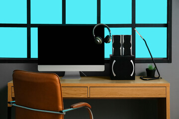 Workplace with modern computer, speakers and headphones near grey wall