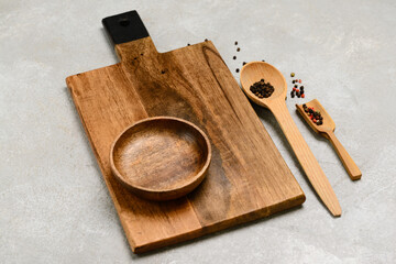 Wooden cutting board, bowl and spoons on grey background