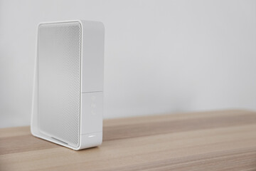 Modern white wi-fi router on table near light wall
