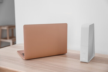 Modern laptop and wi-fi router on table near light wall - obrazy, fototapety, plakaty