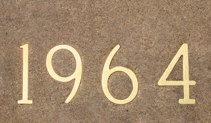 The numbers 1964 in brass embedded  in concrete background