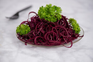 Beets salad, spiralized, decorated with parsley on marble table and glass plate, ready to be...