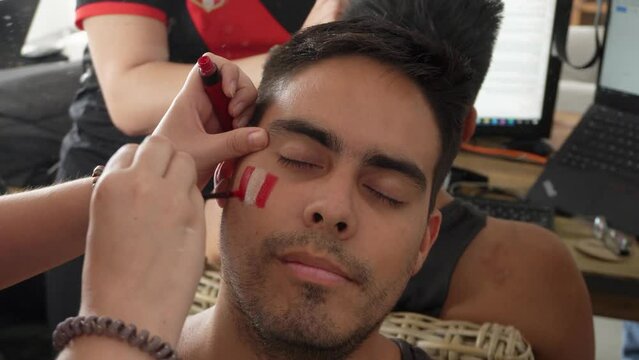 close-up painting the face of a man with the flag of Peru as a sign of fans before a soccer game in the room with friends during the day in 4k