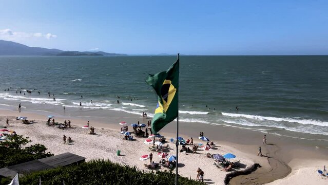 Aerial drone image of brazil flag hoisted fluttering in the wind at coastline flag on the beach