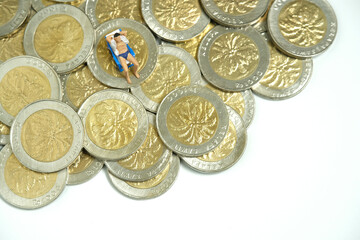 Miniature people toy figure photography. Budget and Financial Plan for travel. Men relaxing seat at beach chair with money coin pile, isolated on blue background