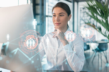 Attractive businesswoman in white shirt at workplace working with laptop to hire new employees for international business consulting. HR, social media hologram icons over office background
