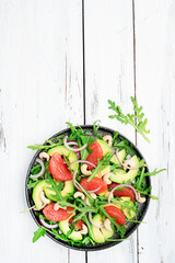 Healthy vegan salad with arugula, avocado, pink grapefruit, cashew nuts and dressing of olive oil, honey and wine vinegar. White rustic kitchen table, top view, negative space
