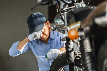 Male tired working in repair shop, wiping off sweat after working, mechanic repairing motorcycle,...