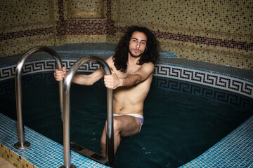An attractive guy with long hair is relaxing in the pool. Relaxation and pleasure.