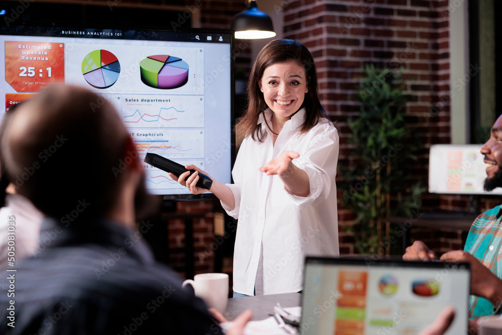 Poster smiling business employee standing in front of tv screen with sales statistics talking with man with