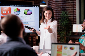 Smiling business employee standing in front of tv screen with sales statistics talking with man...