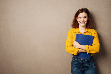 Laughing young woman against a brown background with her application documents in her hands - 505083249
