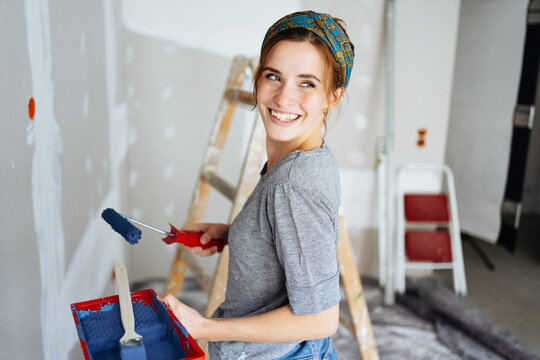 Young happy woman paints her apartment and looks back