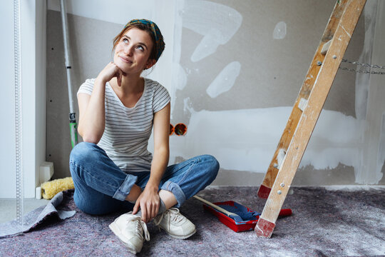 Young woman sitting in her unrenovated apartment thinking how to paint the walls