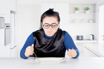 Fat woman eating with empty plate at home