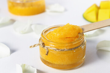 Orange color sugar scrub with mango pieces on a white table front view.