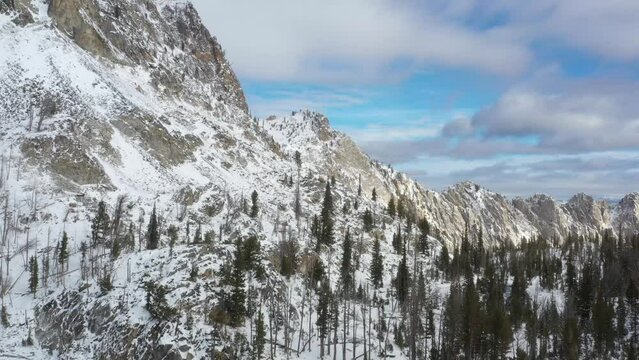 Drone clip of snowy alpine nature and peaks. It's beautiful with blue skies and poofy clouds of idaho pine trees