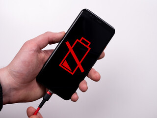 Smartphone is connected to the charger on a white background top view. Discharged battery. Low...