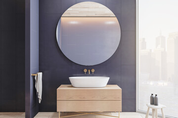 Front view on round mirror in grey wall above wooden sink base cabinet and big window with city...