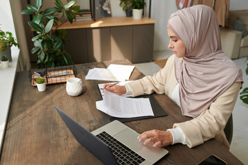 Horizontal high angle view shot of young Middle Eastern woman in hijab working with financial...