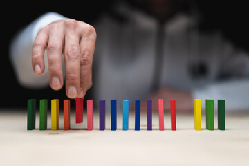 Conceptual photo of a hand placing a stone to a row of domino stones.
Domino effect with colored stones and copyspace