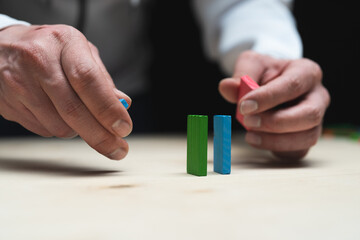 Conceptual photo of hands preparing a row of domino stones.
Domino effect with colored stones and...