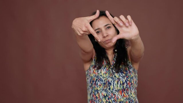 Creative indian model pretending to take picture in studio, doing frame shape with fingers in front of camera. Capture photography image with focus view, capturing moment of imagination.