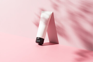 white cosmetic tube for face or body cream, cleanser or shampoo on a pink background with leaves...