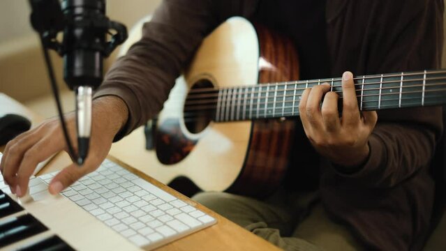 Close up hand Professional songwriter playing guitar with tablet and audio equipment for Mixing and Mastering music. Male composing a song with piano keyboard at Recording studio. Musician concept