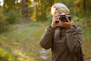 Young woman taking photo on film camera in forest 