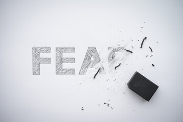 Word hand writing FEAR is deleted by black eraser on white paper background copy space. No fear or...