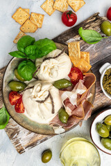 Antipasto burrata cheese salad served with cherry tomatoes, fresh basil leaves, prosciutto ham and olives. prosciutto, mozzarella. vertical image. top view. place for text