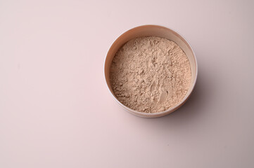 Mineral loose powder in a open cosmetic round jar on a pink background with copy space. Top view....