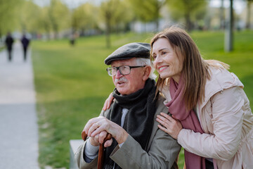 Happy senior with his adult daughter sitting outdoors in park.