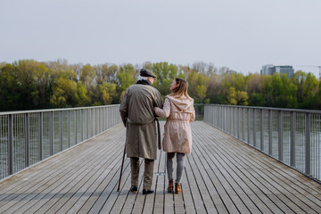 Rear view of senior man with daughter outdoors on a walk on pier by river.