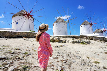Young woman walking among traditional greek windmills on Mykonos island, Cyclades, Greece - obrazy, fototapety, plakaty