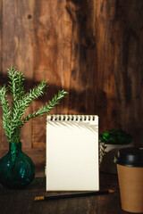 blank sprial notebook with home plant on wood table with sunlight from window