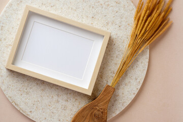 blank photo frame with pampas grass on marble stand at peach table