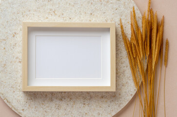 blank photo frame with pampas grass on marble stand at peach table