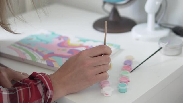 A woman paints a picture with acrylic paints according to the house numbers.