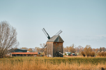 Fototapeta na wymiar Wooden windmill stands on a coastline of a canal. Spring landscape of a rural area in Poland