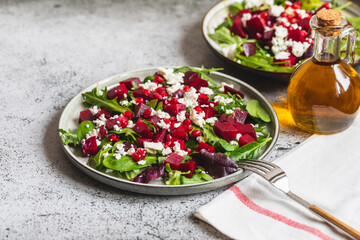 Arugula, Beet and cheese salad with pomegranate and dressing on plate on grey stone kitchen table...